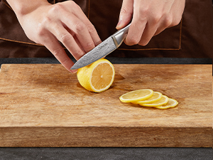 Trancher à la main un citron en fines rondelles sur une planche à découper en bois, en faisant la démonstration du travail au couteau sur les agrumes