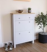 Meuble à chaussures blanc avec plateau en bois naturel, avec trois tiroirs à poignées argentées, décorés avec des plantes en pot et placés contre un mur beige