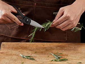 Les mains utilisent des ciseaux de cuisine pour couper des herbes fraîches sur une surface de planche à découper en bois.