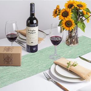 Service de table avec bouteille de vin, verres, tournesols dans un vase et service de table. Nappe verte visible. Boîte en bois dans le coin de l'image.