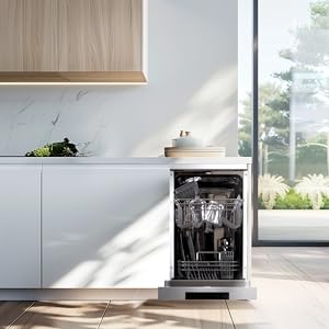 Cuisine moderne avec armoires blanches, étagères supérieures en bois et lave-vaisselle ouvert avec verrerie propre. Grande fenêtre avec vue extérieure visible.