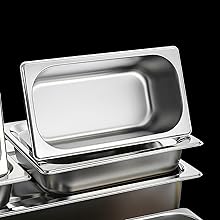 Casseroles de restauration en acier inoxydable empilées, avec le couvercle du plateau supérieur partiellement ouvert. Les casseroles ont une forme rectangulaire profonde avec des coins arrondis.