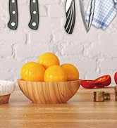 Scène de cuisine avec un bol en bois rempli d'oranges. Des ustensiles de cuisine, un tissu à carreaux bleus et des vues partielles d'autres ingrédients sont visibles