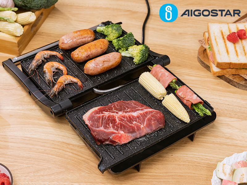 représentant de la viande, des saucisses, des crevettes et des légumes grillés répartis sur deux surfaces de cuisson antiadhésives