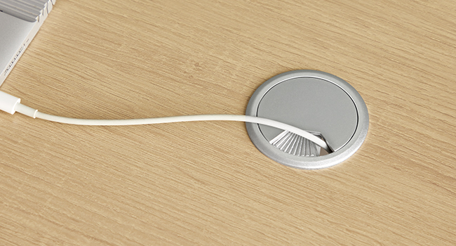 avec fonction de gestion des câbles. Construction en plastique blanc avec couvercle à charnière, installée sur une surface en bois clair