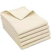 Pile de cinq serviettes pliées en tissu de couleur crème. Les serviettes semblent être faites d'un tissu texturé avec un motif côtelé visible. Une serviette sur le dessus est partiellement dépliée pour montrer sa forme carrée