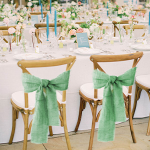 Deux chaises de salle à manger en bois avec des nœuds en ruban vert attachés au dossier, installées pour un événement officiel ou une réception de mariage.