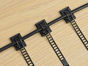 Gros plan sur des serre-câbles noirs attachés à une longue tige noire. Les attaches ont un design en forme d'échelle et sont fixées à une surface en bois clair