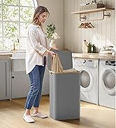 Femme plaçant des vêtements dans un panier à linge gris dans la cuisine avec machine à laver et sèche-linge visibles