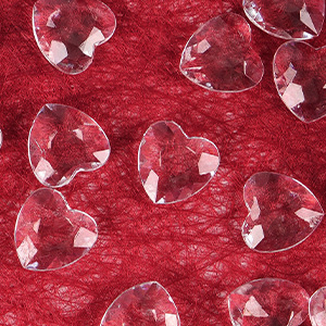 Éléments décoratifs en cristal ou en acrylique en forme de cœur à multiples facettes disposés sur un fond texturé rouge