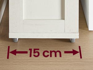 Gros plan des pieds de meubles sur le plancher en bois. La flèche rouge indique une largeur de 15 cm entre les pieds peints en blanc. Pieds en métal ou en plastique visibles sous les pieds.