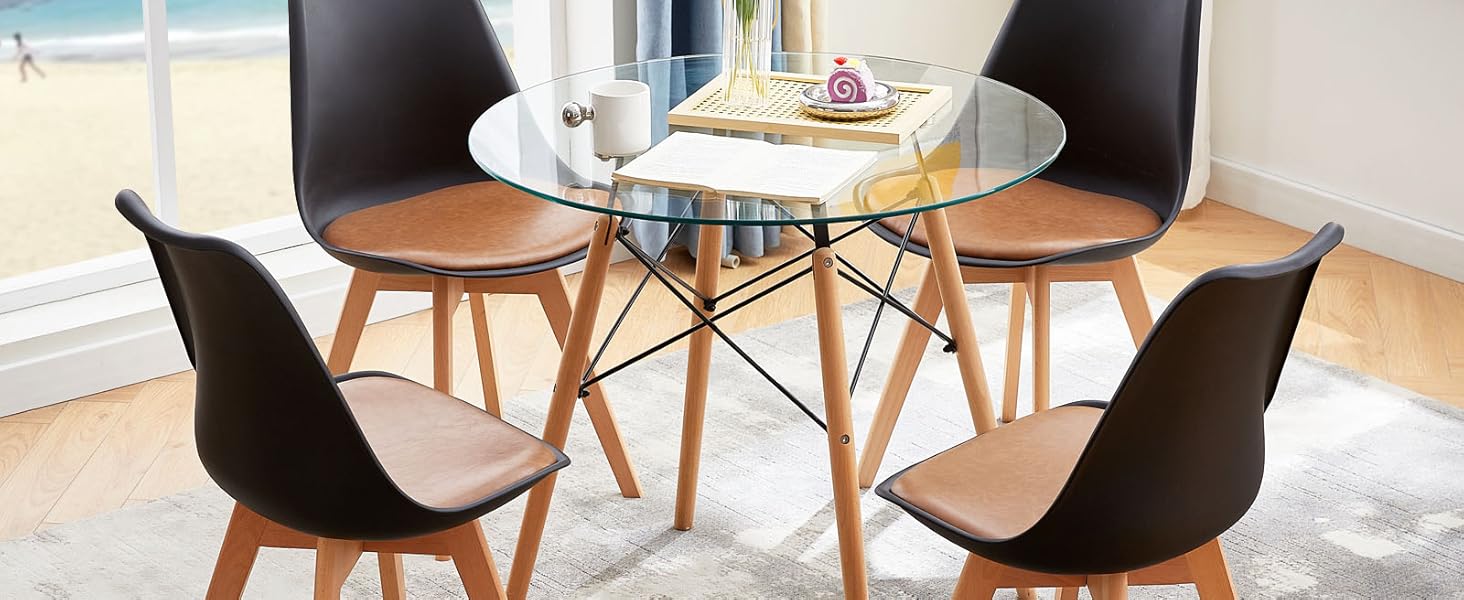 avec table ronde en verre et quatre chaises noires avec pieds en bois, posées sur un tapis gris près des fenêtres.