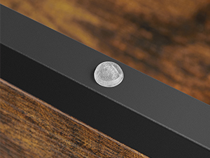 Gros plan d'un objet en métal noir avec un bouton ou un emblème circulaire en argent. L'objet semble reposer sur une surface en bois.