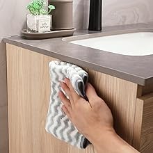 une main tenant une serviette au-dessus du lavabo d'une salle de bain.