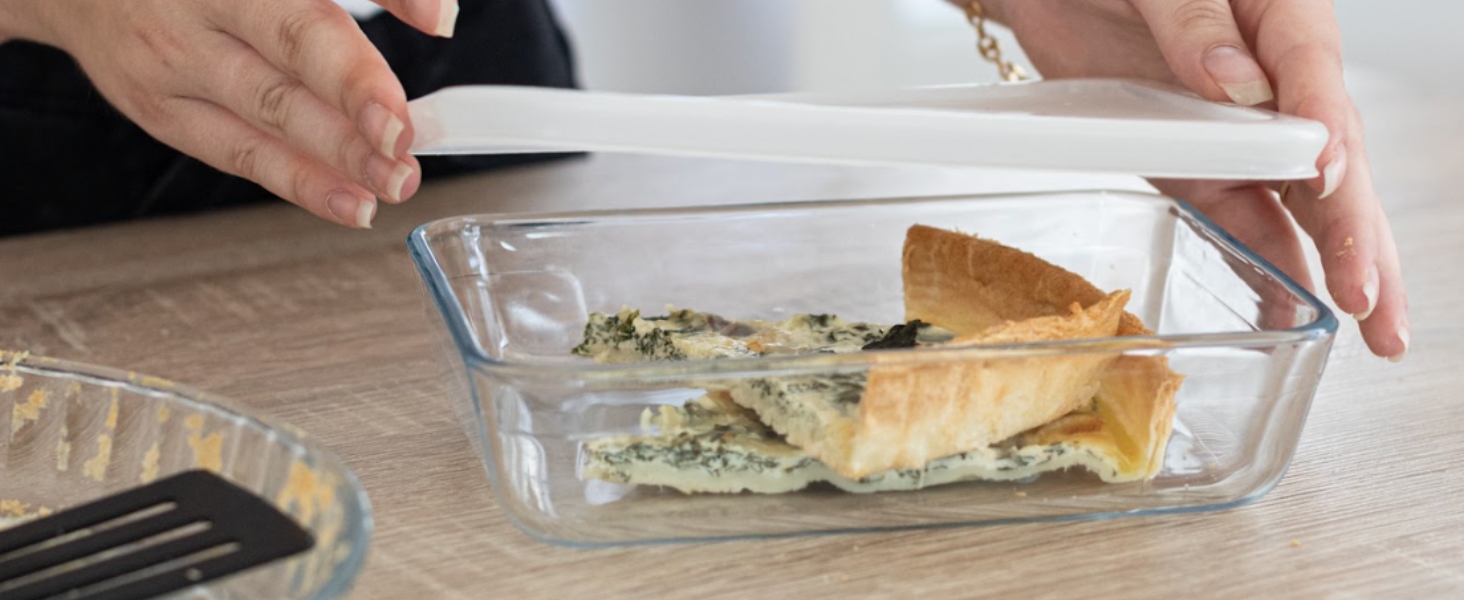 Les mains placent un couvercle blanc sur un récipient en verre contenant de la nourriture. Le contenant contient ce qui semble être une pâtisserie ou une tarte partiellement consommée.