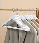 Cintres en bois blancs sur une tringle de placard contenant des vêtements de couleur claire. Les cintres sont dotés d'épaules plates et larges pour soutenir les vêtements