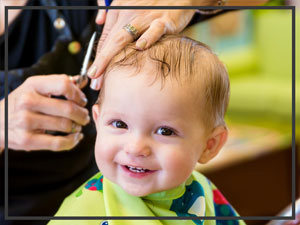 Un jeune enfant assis dans un fauteuil de coiffure se fait couper les cheveux, souriant tout en se faisant couper les cheveux avec des ciseaux professionnels