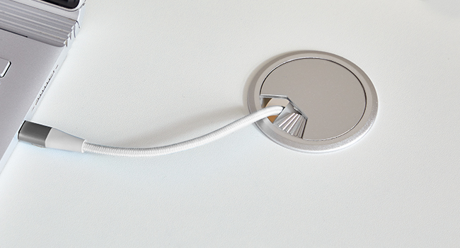 Gros plan d'une solution de gestion des câbles élégante et moderne. Un cordon blanc passe à travers une ouverture circulaire dans ce qui semble être la surface d'un bureau ou d'une table.