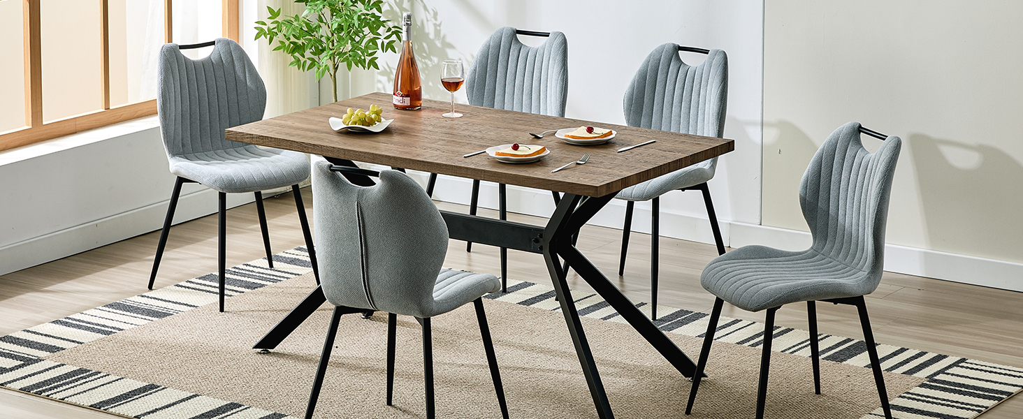 avec table en bois rustique et quatre chaises capitonnées grises sur des pieds en métal noir, posées sur un tapis à motifs géométriques