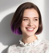 Portrait professionnel montrant une personne en tenue de couleur claire avec des cheveux mi-longs coiffés de reflets violets.