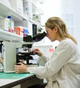Cadre de laboratoire avec microscope et équipement scientifique sur des étagères, avec une personne en blouse blanche menant des recherches.