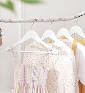 Cintres en bois blanc sur une branche. Les vêtements suspendus comportent des motifs floraux et à pois. Couleurs pastel et neutres visibles.