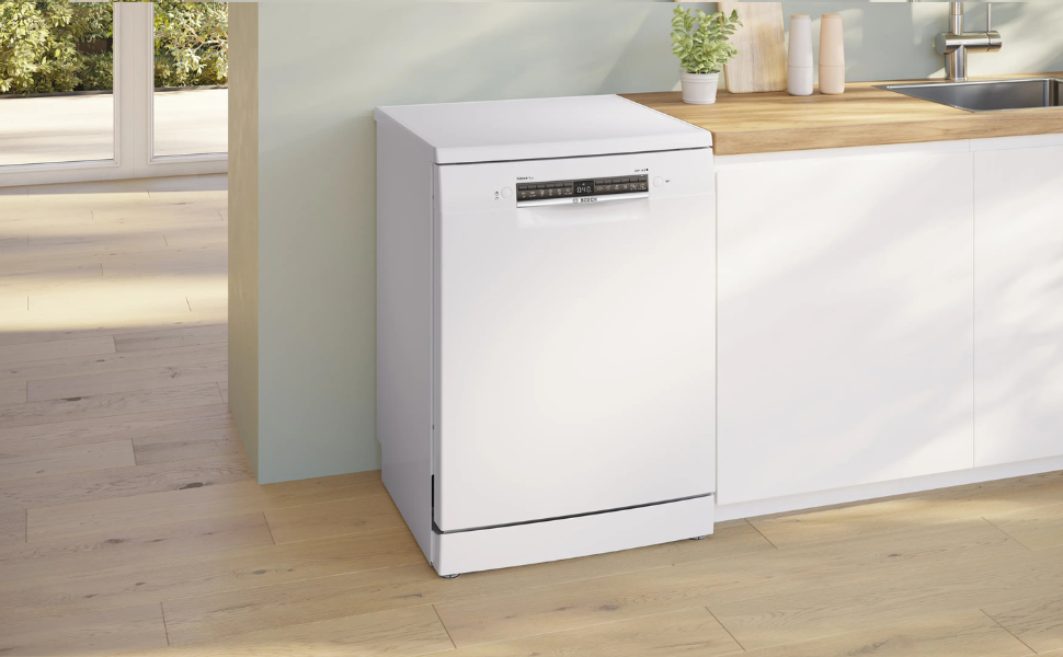 Lave-vaisselle autoportant blanc au design moderne, positionné contre un mur blanc avec plan de travail en bois visible. Dispose de lignes épurées et d'un panneau avant minimaliste avec poignée.