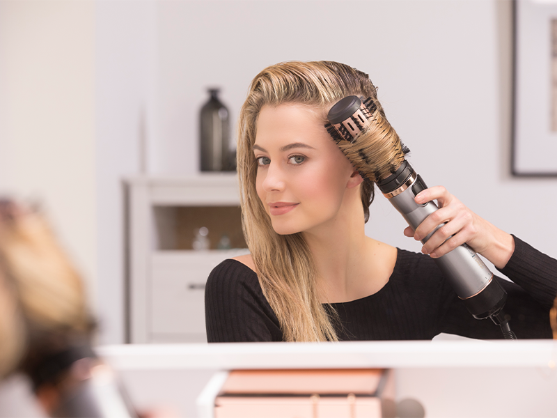 Personne coiffant les cheveux avec un outil de coiffure professionnel en salon, portant des rouleaux tout en utilisant un appareil de coiffage.