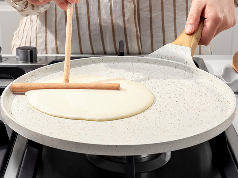 Les mains utilisent des outils en bois pour étaler et façonner une pâte fine sur une grande surface de cuisson ronde et plate.