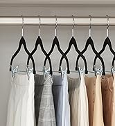 Rangée de cintres à pantalons noirs à clips, contenant divers échantillons de tissus ou vêtements de couleur claire sur fond blanc