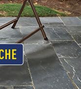 Pieds de trépied en bois sur un patio en pierre grise. Panneau jaune avec une partie du texte « CHE » visible au premier plan.