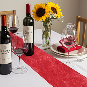 Décoration de table élégante avec des bouteilles de vin, des verres à vin, un chemin de table rouge et des tournesols dans un vase en verre sur une nappe blanche