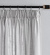 Tringle à rideau noire avec embout doré, supportant des rideaux gris clair avec bordure plissée en crayon. La tringle est dotée de six anneaux de suspension visibles. Les rideaux semblent texturés et semi-transparents