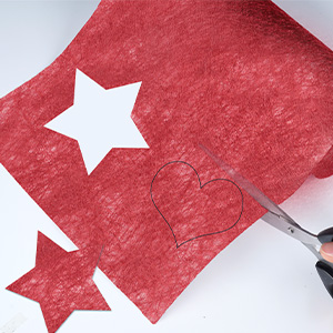 Papier ou tissu texturé rouge avec des formes d'étoiles blanches découpées et des ciseaux visibles dans le cadre