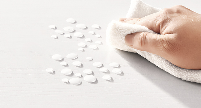 De petites pilules blanches éparpillées sur une surface blanche. Une main tenant un chiffon, peut-être pour nettoyer ou essuyer les pilules.