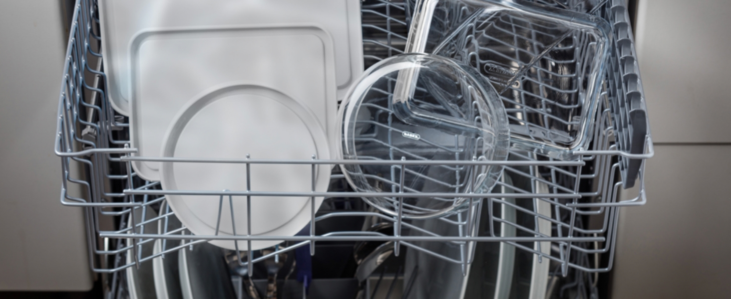 Vue intérieure d'un lave-vaisselle rempli d'assiettes blanches, de bols et d'un récipient en verre transparent. Supports métalliques et porte-ustensiles visibles.