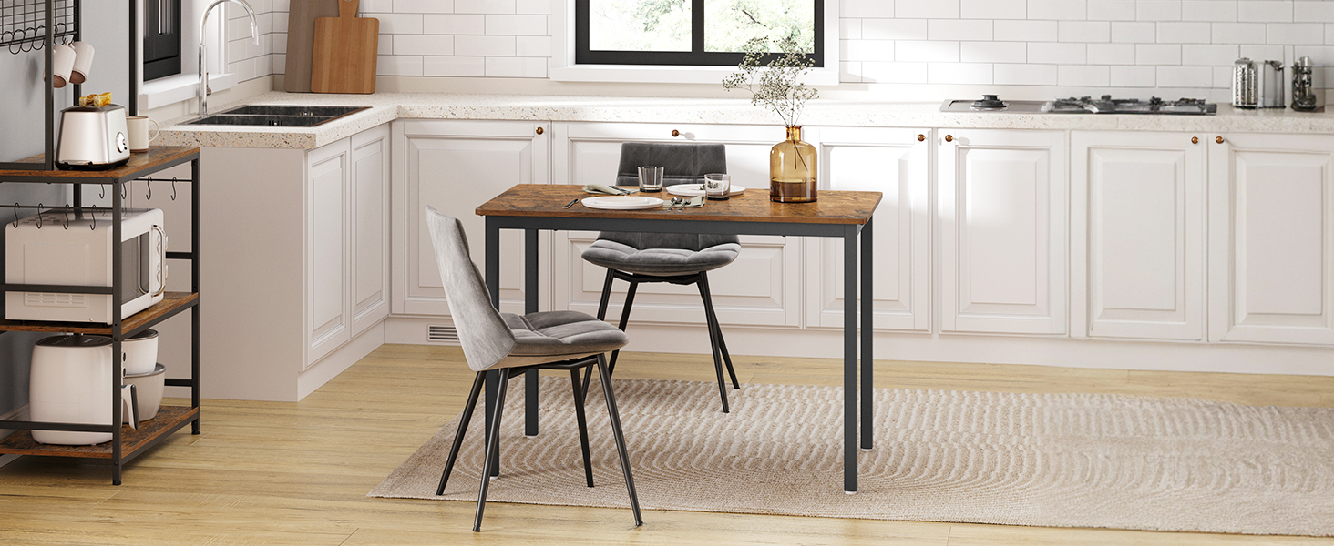 Cuisine moderne avec armoires blanches, table ronde en bois, deux chaises grises et parquet. Table adossée à un mur surmontée de fenêtres.