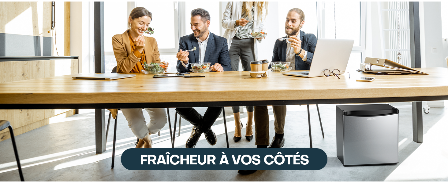 Trois personnes assises à une grande table en bois dans un bureau. Un appareil compact en argent, peut-être un purificateur d'air, est visible sous la table.