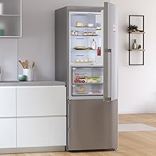 Réfrigérateur moderne en acier inoxydable avec porte vitrée dans un décor de cuisine blanc contemporain, avec des étagères intérieures organisées avec des produits alimentaires.