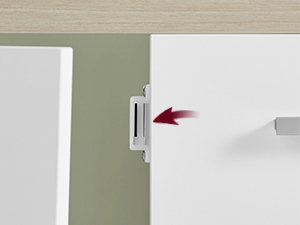 Gros plan d'un loquet ou d'un mécanisme de verrouillage magnétique blanc monté sur un mur, avec une flèche rouge indiquant la direction