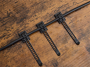 Trois serre-câbles en plastique noir fixés à une tige métallique sur une surface en bois patinée. Les attaches sont dotées d'un mécanisme à cliquet pour un serrage ajustable