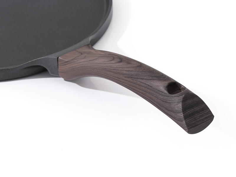 Gros plan d'une surface de cuisson circulaire gris foncé à laquelle est attaché un manche en bois, probablement une partie d'un appareil de cuisine ou d'un ustensile de cuisine