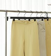 Porte-vêtements avec cintres pouvant contenir un pantalon ou un pantalon jaune clair et beige. Une tige métallique soutient les vêtements, mettant en valeur une sélection de garde-robe minimaliste