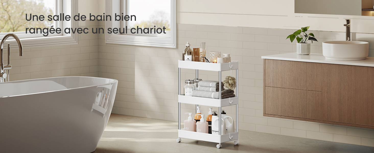 Le texte se lit comme suit : « Une salle de bain bien rangée avec un seul chariot ». Intérieur de salle de bain moderne avec baignoire autoportante et chariot blanc à 3 niveaux contenant les essentiels de la salle de bain contre des murs carrelés beiges.