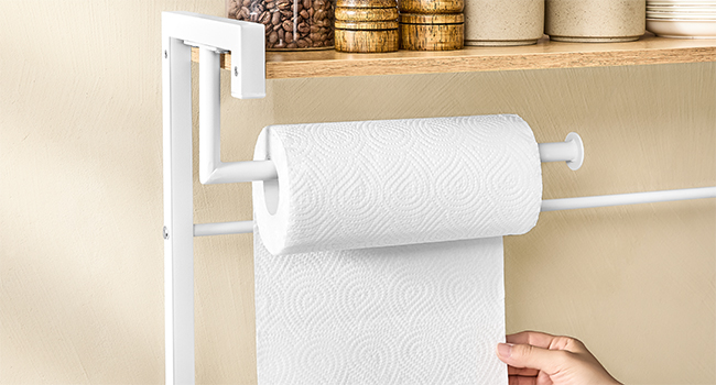 Porte-essuie-tout en métal blanc fixé sous une étagère en bois. Tirer la feuille du rouleau à la main. Récipients décoratifs visibles sur l'étagère ci-dessus.