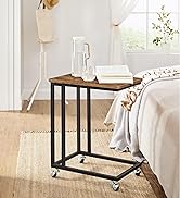 avec plateau en bois et structure en métal noir sur roulettes. Placé à côté d'un canapé avec des objets décoratifs sur le dessus.