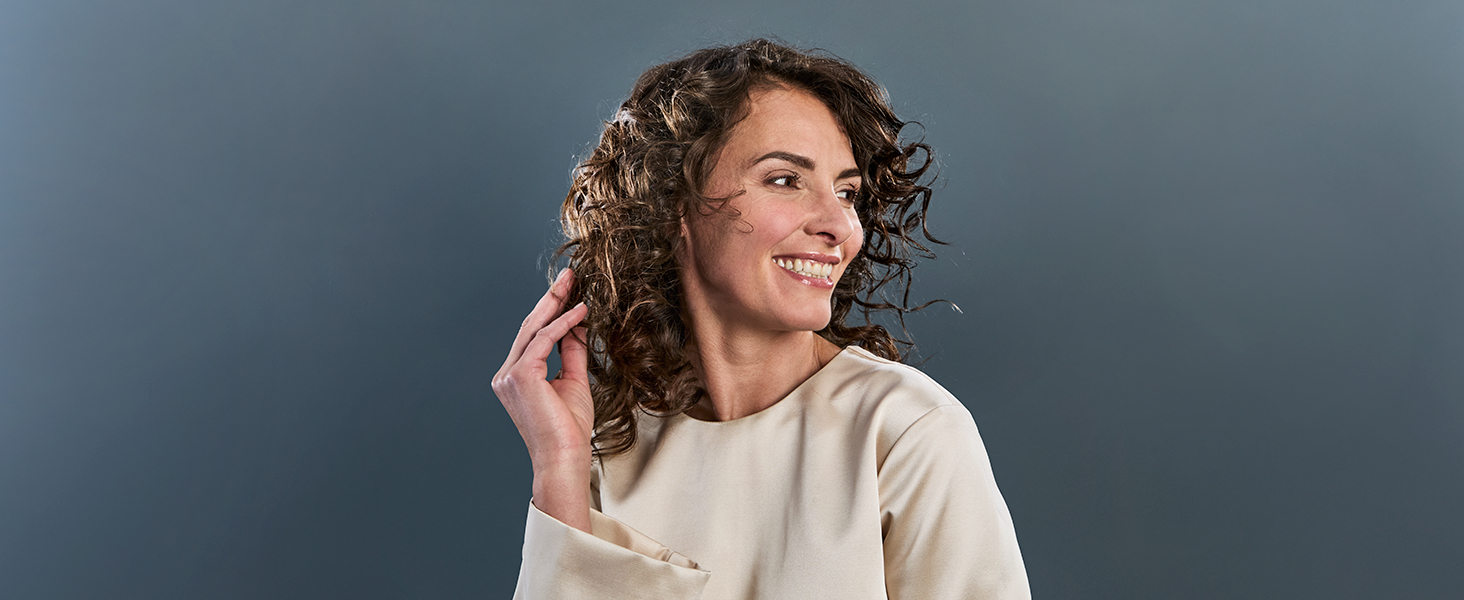 Personne en pull blanc décontracté sur fond gris, faisant la démonstration d'un produit d'écoute ou lié à l'audio.