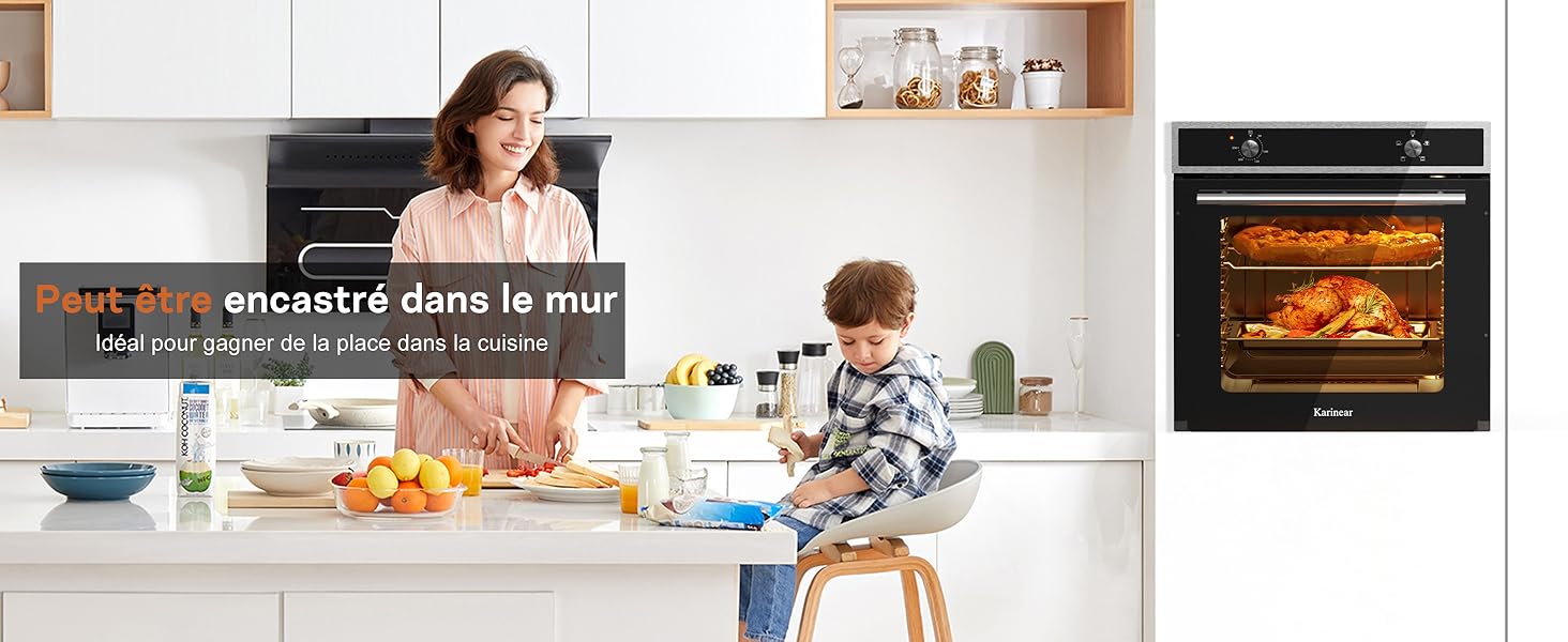 Scène de cuisine avec four mural intégré affichant du poulet rôti. Armoires blanches, comptoir avec fruits et petits appareils électroménagers visibles. Le four a une porte vitrée montrant un intérieur éclairé.
