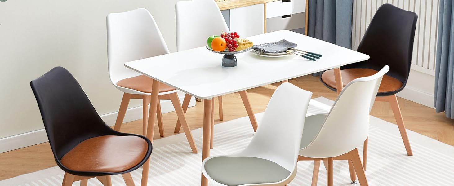 avec table rectangulaire blanche et six chaises. Quatre chaises blanches et deux chaises noires avec pieds en bois. Cette chambre dispose d'une fenêtre, de rideaux et d'œuvres d'art mural.