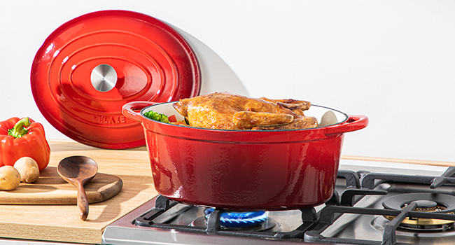 Four hollandais en fonte émaillée rouge sur cuisinière à gaz, contenant du pain. Couvercle à proximité, avec légumes et planche à découper au premier plan.